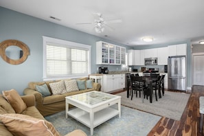 A modern kitchen with white cabinets, a stainless steel refrigerator, and a dining area with a glass coffee table.