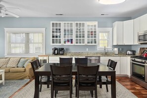 Una cocina moderna con armarios blancos, una mesa de comedor con sillas, una estufa y una cafetera.