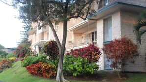 Un edificio su due piani con un balcone, circondato da giardini curati e un'area di parcheggio.