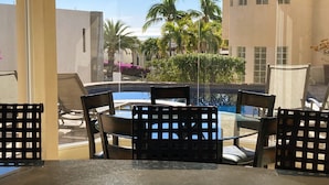 Ein verglaster Balkon mit Billardtisch und Stühlen, mit Blick auf einen Pool und Palmen.