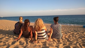 Vier Personen sitzen am sandigen Strand und blicken auf das Meer.