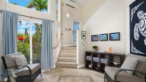 Amplia sala de estar con una mesa de centro de vidrio, dos sillones, un sofá, una escalera y vistas al exterior.