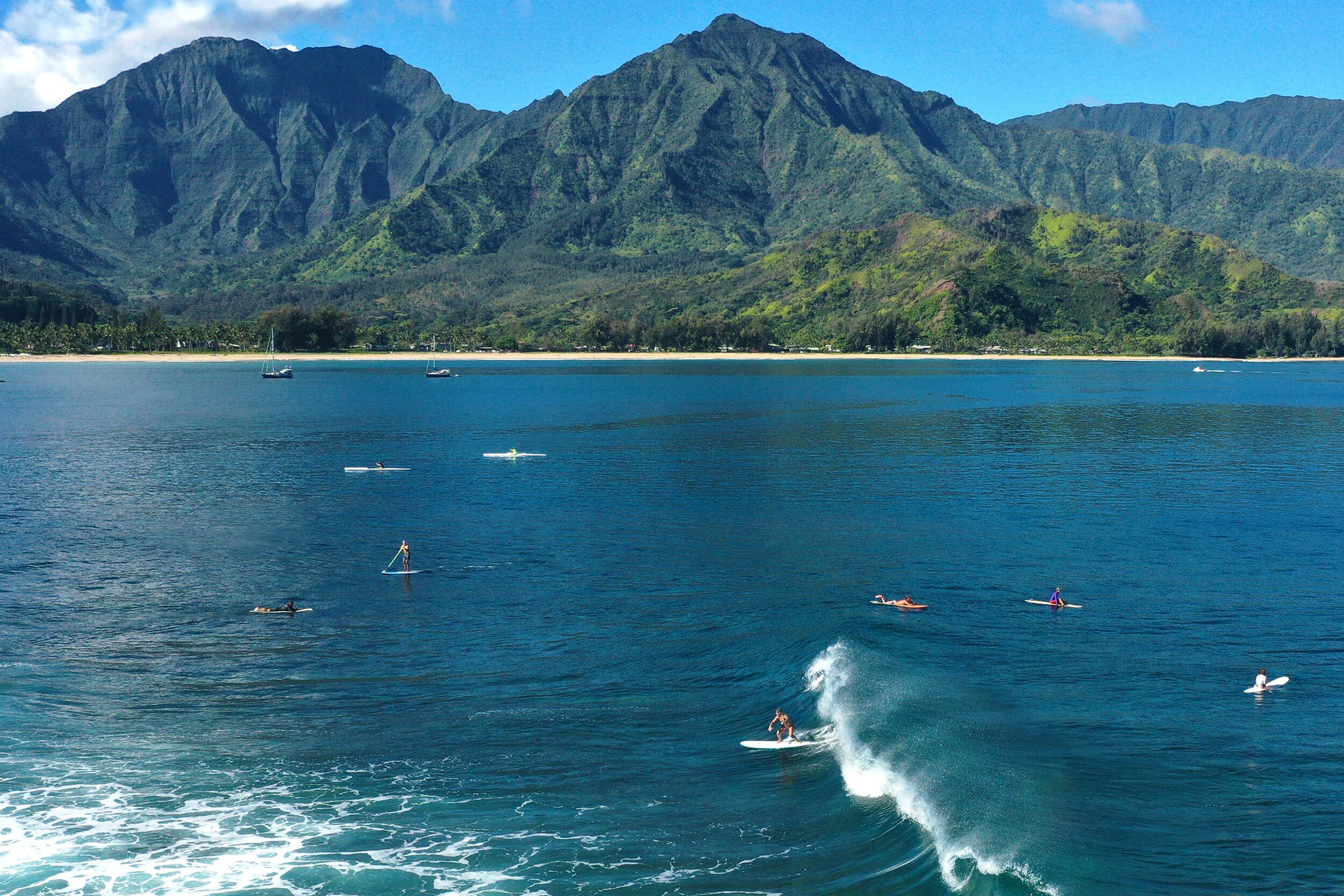 A coastal view with a mountain range in the background, calm water, and several boats.