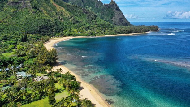 Una playa tropical con aguas turquesas cristalinas, montañas verdes exuberantes y una costa arenosa.