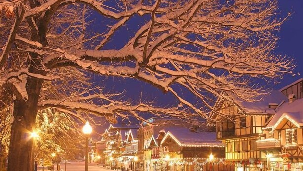 A snow-covered street lined with traditional buildings, illuminated by street lamps.