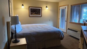 A bedroom with a bed, bedside lamp, framed artwork, and a window with blinds.