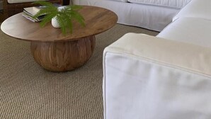 A living room with a white sofa, a wooden coffee table, a wicker chair, and a large mirror on the wall. - Family Friendly Island Getaway (Nantucket)