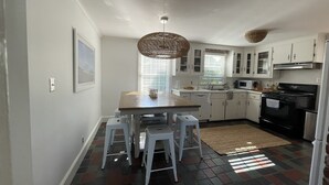 A modern kitchen with white cabinets, a wooden dining table, and a black stove. - Family Friendly Island Getaway (Nantucket)