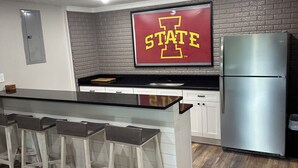 A modern kitchen with a bar area, a stainless steel refrigerator, and a wall-mounted TV displaying "STATE". - Branson area Lakehouse, 5 Bedrooms, 3 Baths, (Sleeps 9-15) New decks Spring 2019 (Kimberling City)