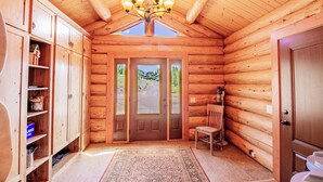 A log cabin interior with a chandelier, wooden cabinets, a chair, and a door leading outside. - Mountain Getaway w/additional Bunkhouse Apartment! (Anaconda)