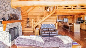 A log cabin interior with a stone fireplace, a leather sofa, a dining area, and a kitchen. - Mountain Getaway w/additional Bunkhouse Apartment! (Anaconda)