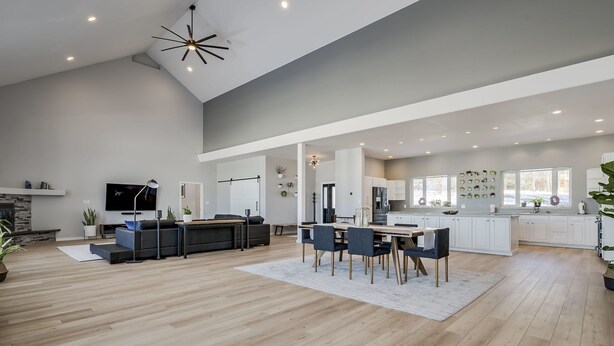 A spacious living area with a dining table, sofas, and a kitchen area with white cabinets and a large window.
