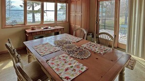 Un comedor con mesa de madera, sillas y vistas al lago a través de amplios ventanales.