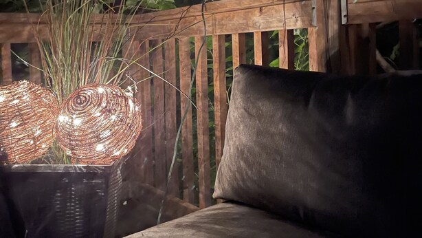 Een houten terras met een comfortabele zithoek buiten, omringd door groen en sfeerverlichting.