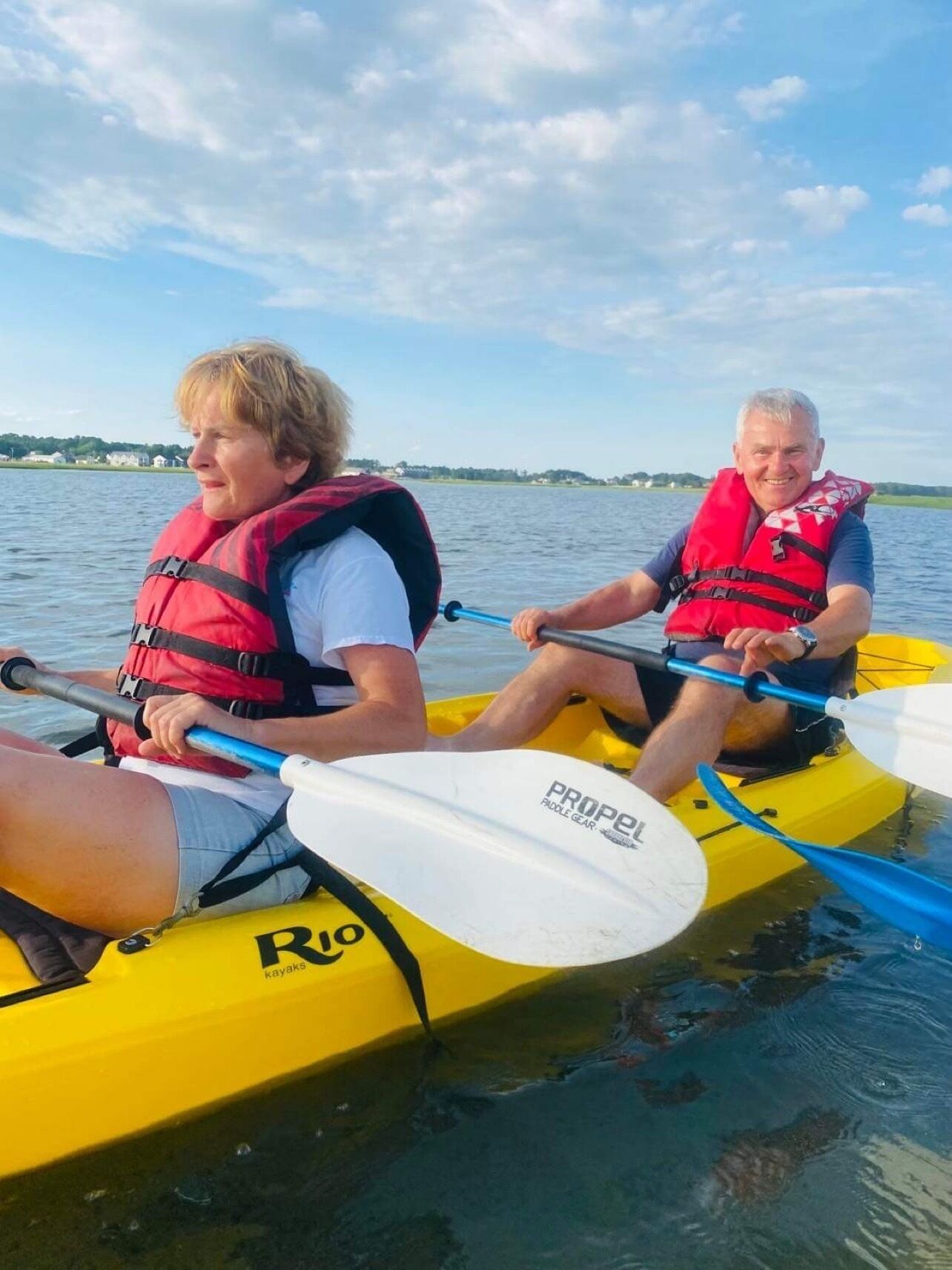 Two people in a yellow kayak with "PROPEL" written on the paddle, wearing life jackets.