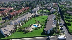 Zona residencial con varios edificios de apartamentos, una piscina y una calle con vehículos.