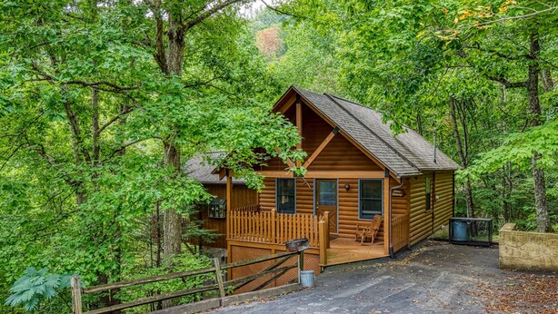 A wooden cabin with a porch and a covered parking area, surrounded by dense forest. - Lake Front with Lake view, King size Bed Great Place to relax and go fishing (Sevierville)