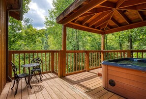 A wooden deck with a hot tub, a table with chairs, and a gazebo overlooking a forested area. - Lake Front with Lake view, King size Bed Great Place to relax and go fishing (Sevierville)