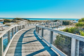 Une promenade en bois dotée d’une rambarde métallique, qui mène à une plage aux eaux d’un bleu limpide.