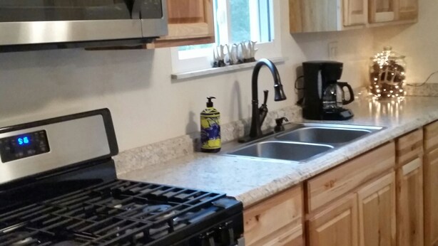 Una cocina con armarios de madera, un microondas de acero inoxidable, una estufa a gas, un fregadero y una ventana.