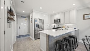 Una cucina moderna con mobili bianchi, elettrodomestici in acciaio inossidabile e una grande isola con sgabelli da bar.