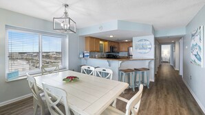 A spacious kitchen with wooden cabinets, a dining area with a white table and chairs, and a view through large windows.