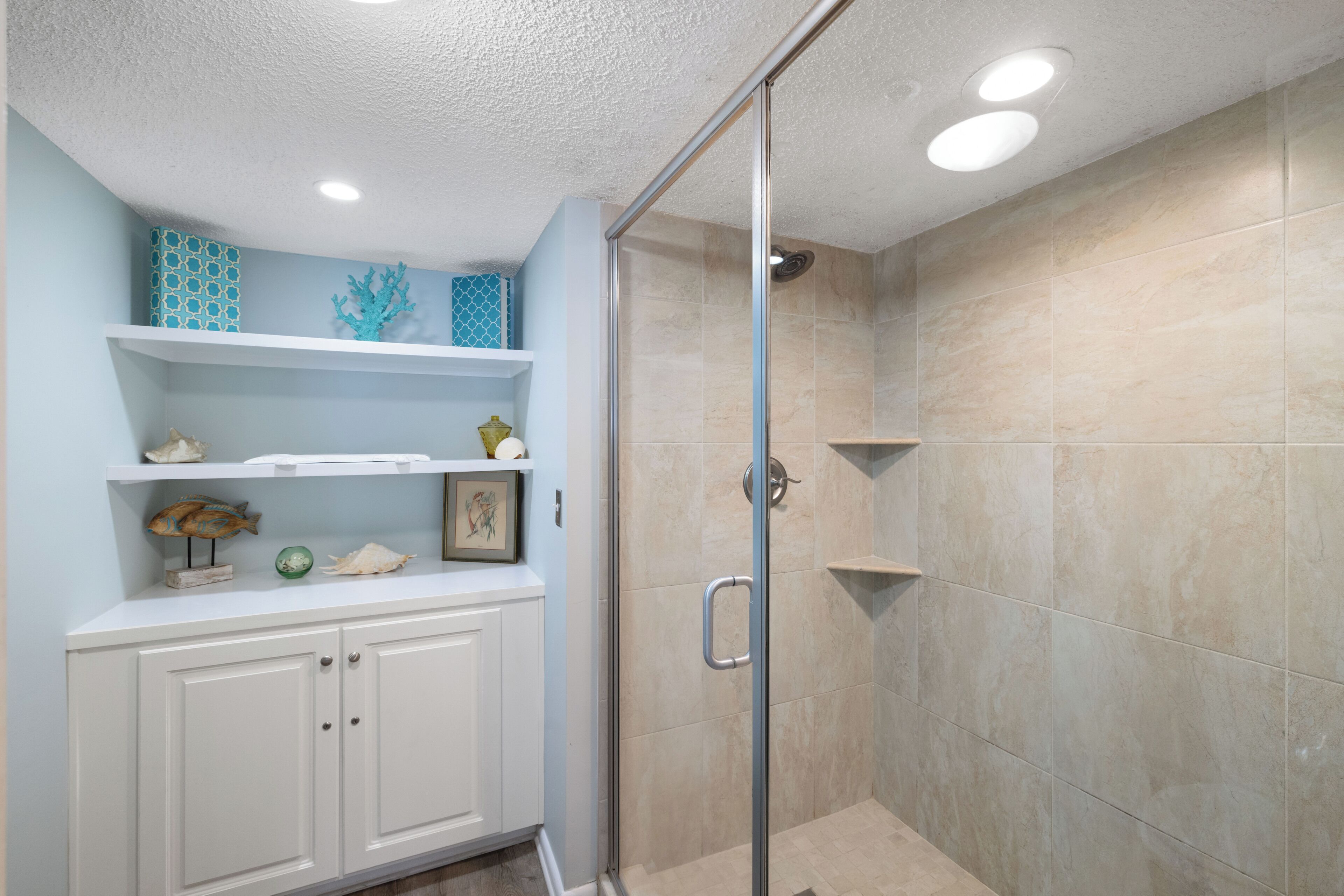 A bathroom with a shower, tiled walls, and a white cabinet with decorative items.