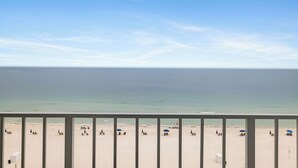 A beach view with a railing in the foreground, a clear sky, and a calm sea.