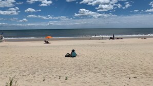 Een strand met een heldere lucht, enkele wolken en een kalme zee. Er zijn een paar mensen en een blauwe tent in het zand.
