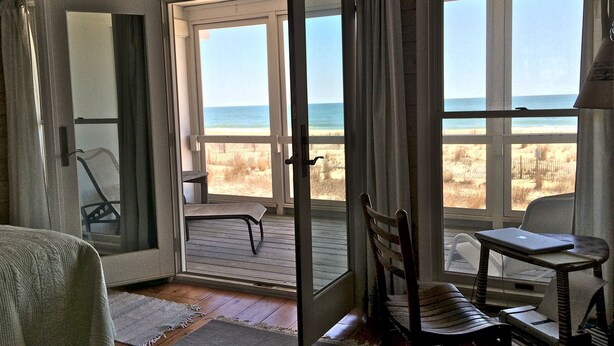 Een kamer met uitzicht op het strand, een houten vloer, een stoel, een tafel en een bed.