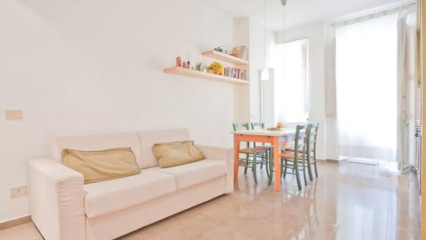 A modern living room with a white sofa, a dining table with chairs, and a kitchen area visible through an open door. - Lovely and Cheap Flat in the Central Area Appio -San Giovanni (rome)