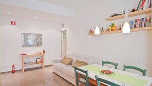 A modern living room with a white sofa, a wooden side table, a dining table with chairs, and a bookshelf with decorative items. - Lovely and Cheap Flat in the Central Area Appio -San Giovanni (rome)