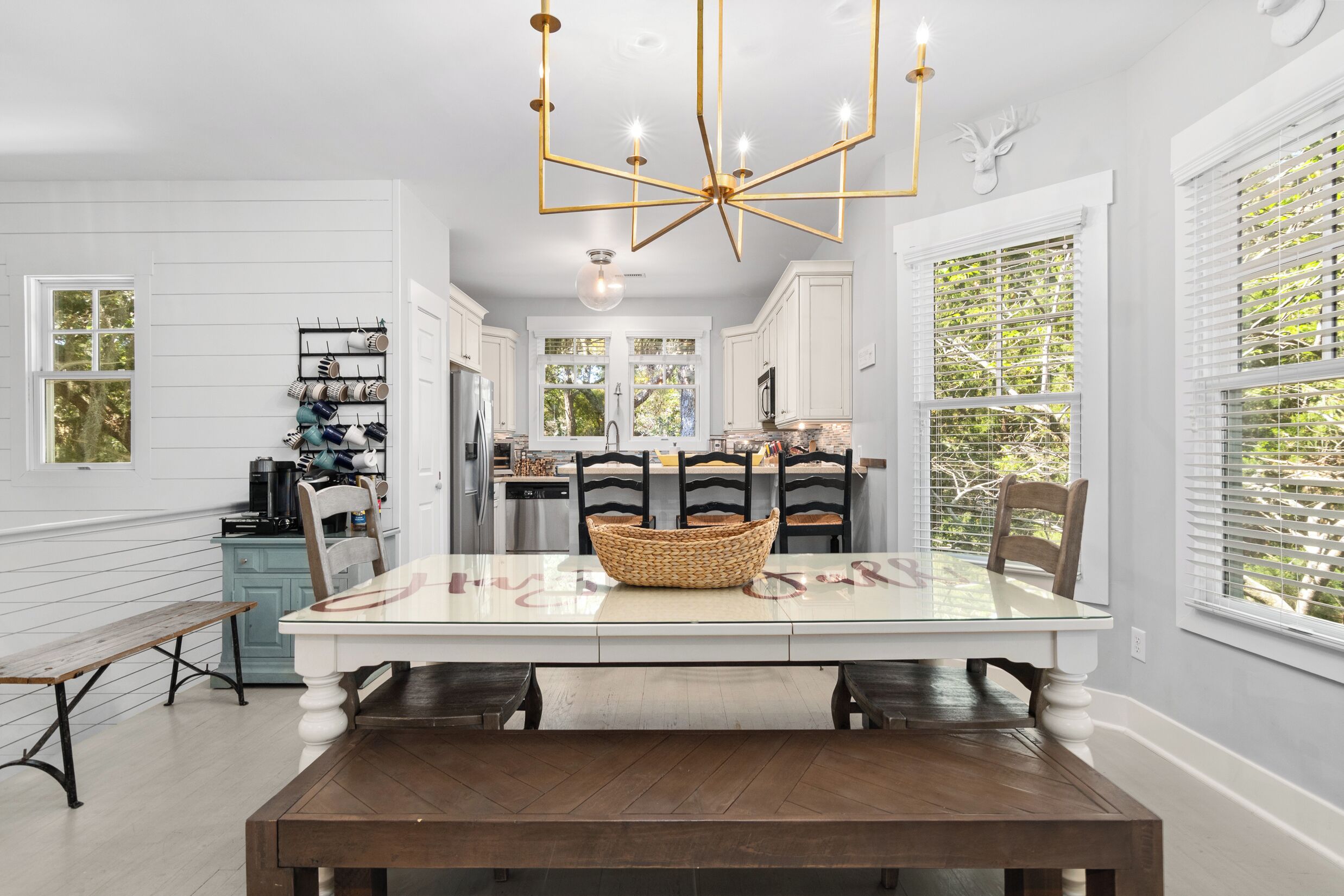 A modern kitchen with white cabinetry, a dining table with chairs, a chandelier, and a view through the windows.