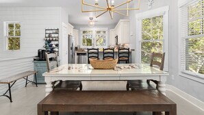 Una cocina moderna con armarios blancos, una mesa de comedor con sillas, una araña y vistas a través de las ventanas.