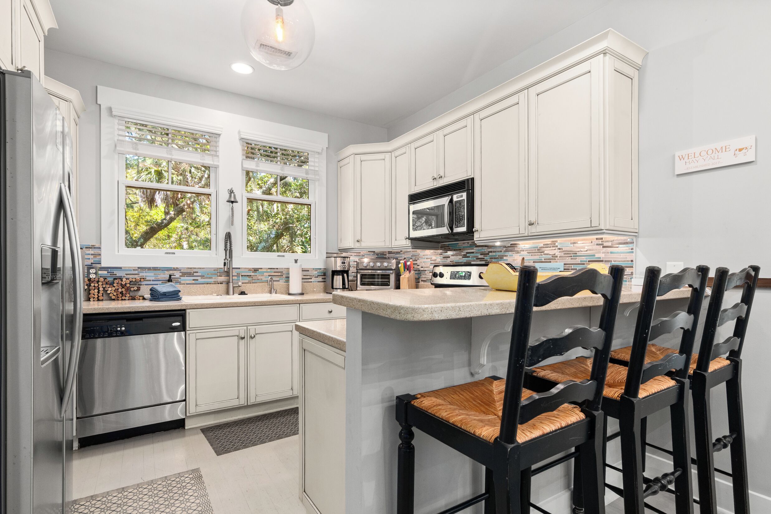 A modern kitchen with white cabinetry, stainless steel appliances, and a breakfast bar with chairs.