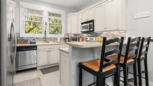 Una cocina moderna con armarios blancos, electrodomésticos de acero inoxidable y una barra de desayuno con sillas.
