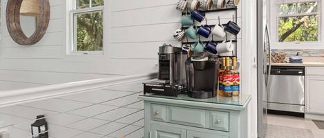 A kitchen with a coffee maker, mugs, and a can of Torani syrup on the counter.