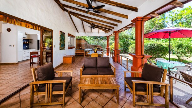 A covered outdoor seating area with wooden furniture, a kitchen in the background, and a red umbrella. - 4 bed / 4 bath w pool and rooftop patio 50m from Beach in Grande (playa grande)