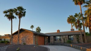 Una casa moderna con fachada de piedra, garaje y jardín frontal ajardinado con palmeras y un cactus.