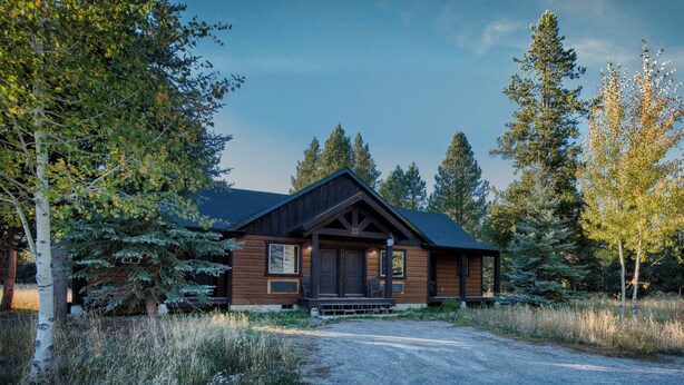 A rustic cabin with a prominent front porch, surrounded by tall trees and a gravel driveway. - Queen Suite at Ponds Lodge Cabin 31 Unit 1 (Island Park)