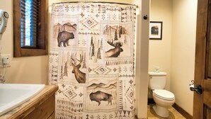 A bathroom with a shower curtain featuring animal prints, a toilet, and a wooden vanity with a sink. - Queen Suite at Ponds Lodge Cabin 31 Unit 1 (Island Park)
