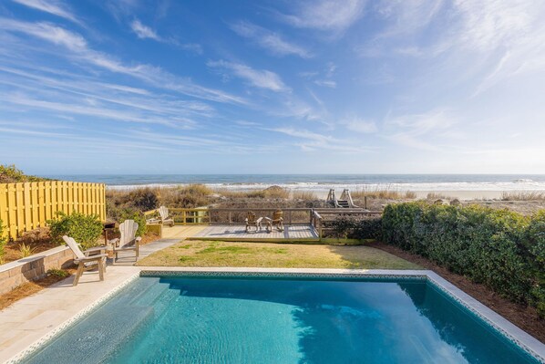 A swimming pool with a deck, chairs, and a view of the ocean.