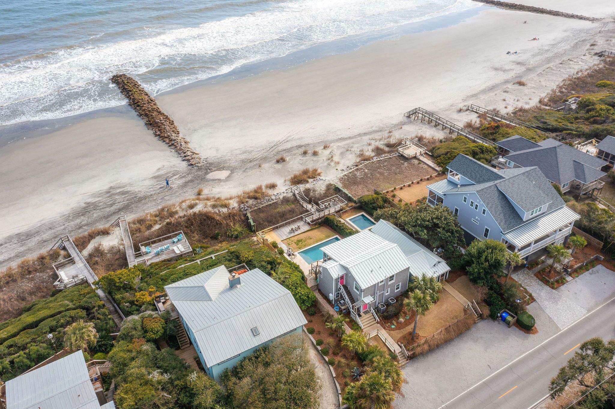 An aerial view of a coastal property with a beach, a swimming pool, and multiple houses.