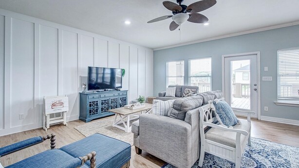 Un salon avec un téléviseur, un meuble bleu, un canapé gris et un ventilateur de plafond.