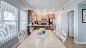 Une cuisine moderne avec des meubles en bois, des appareils électroménagers en acier inoxydable et un coin repas comprenant une longue table et des chaises.