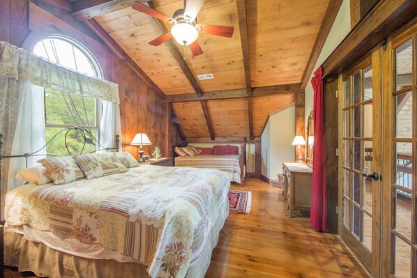 A cozy bedroom with a large bed, two bedside tables with lamps, a wooden ceiling fan, and a window with curtains.
