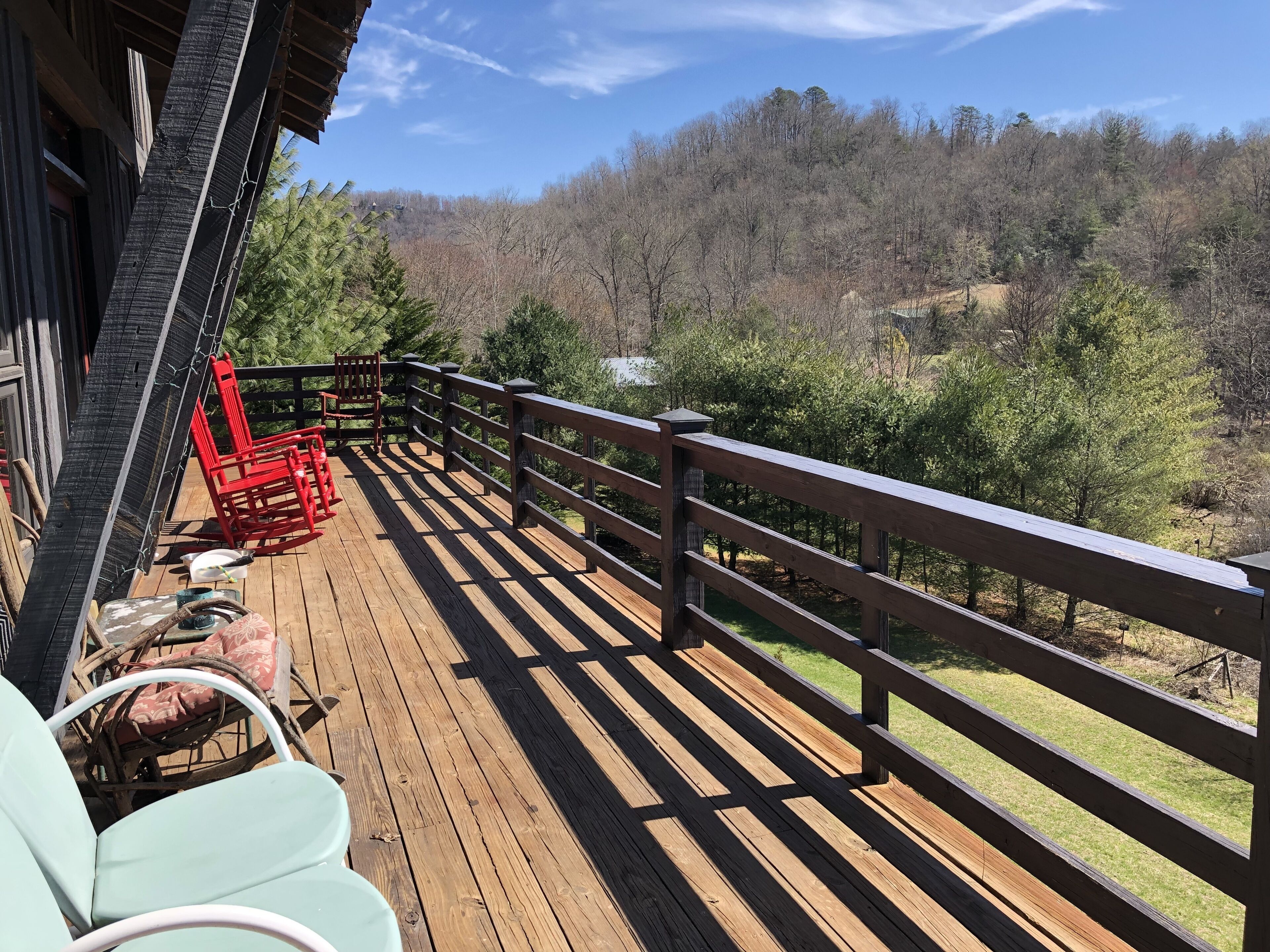 A wooden deck with a railing, red chairs, and a view of a forested hillside.