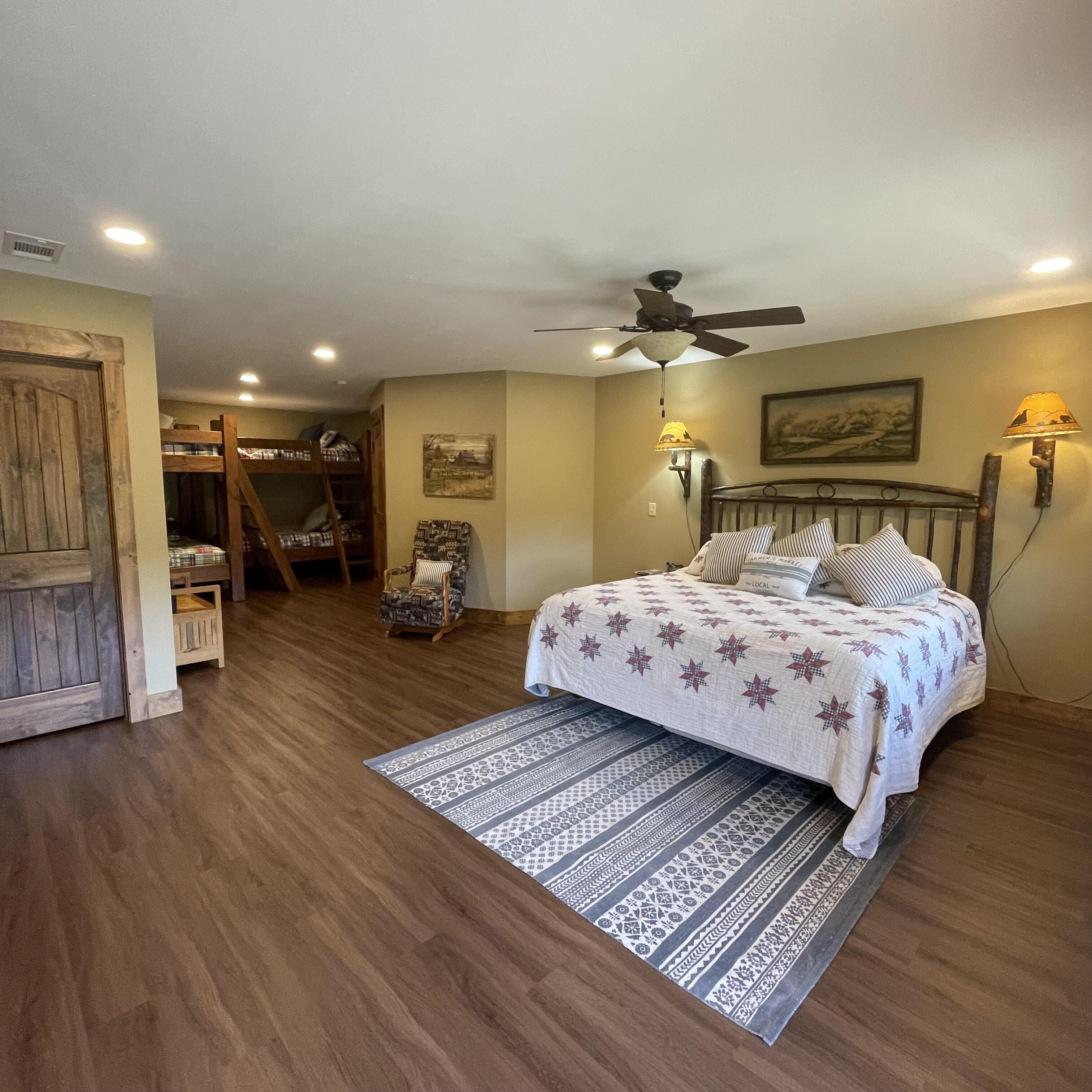 Une chambre à coucher comprenant un lit, un ventilateur de plafond, une table de chevet, une chaise, une porte en bois et une lampe fixée au mur.