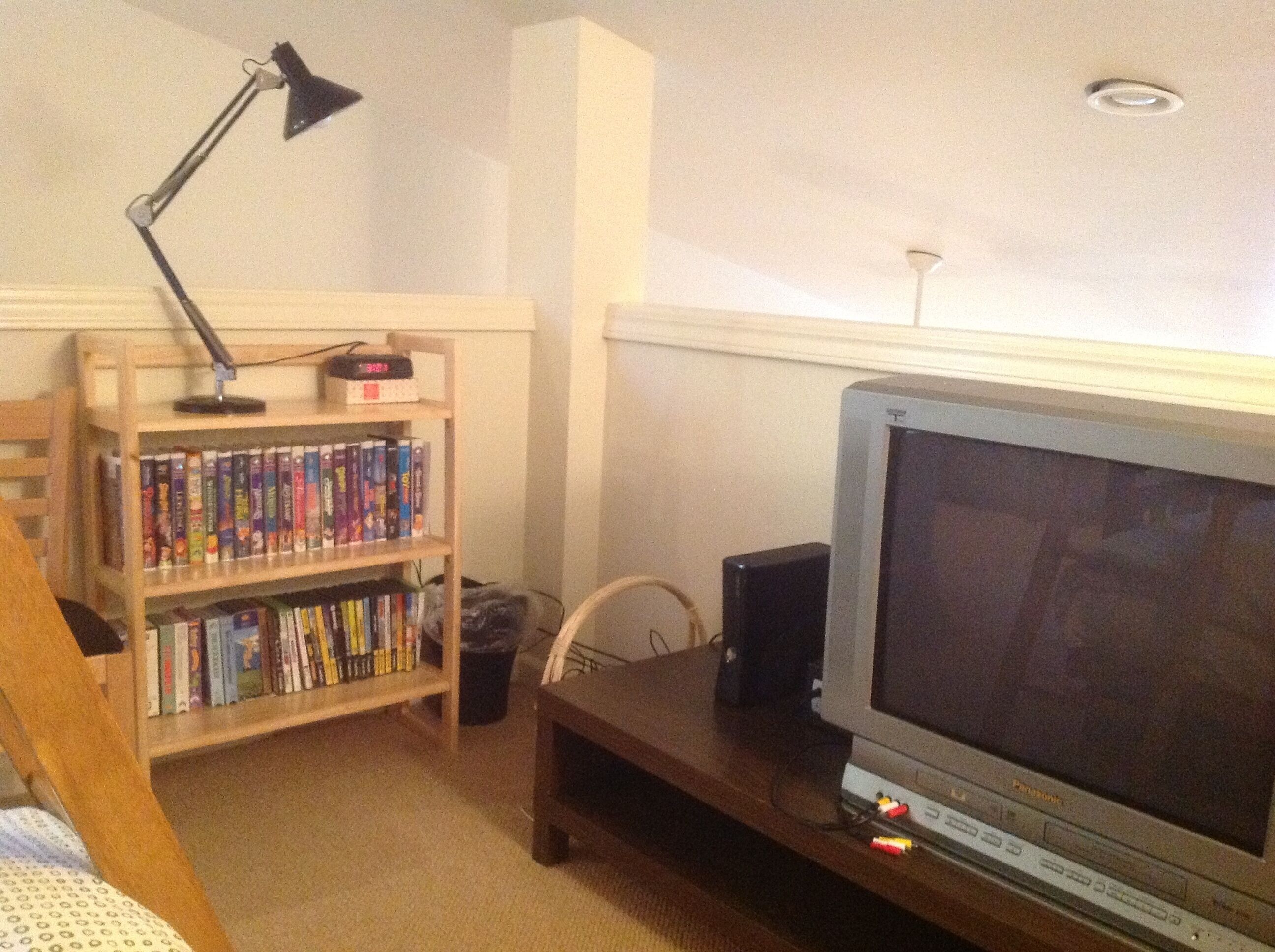 A room with a wooden bookshelf filled with books, a television on a wooden stand, and a desk lamp.