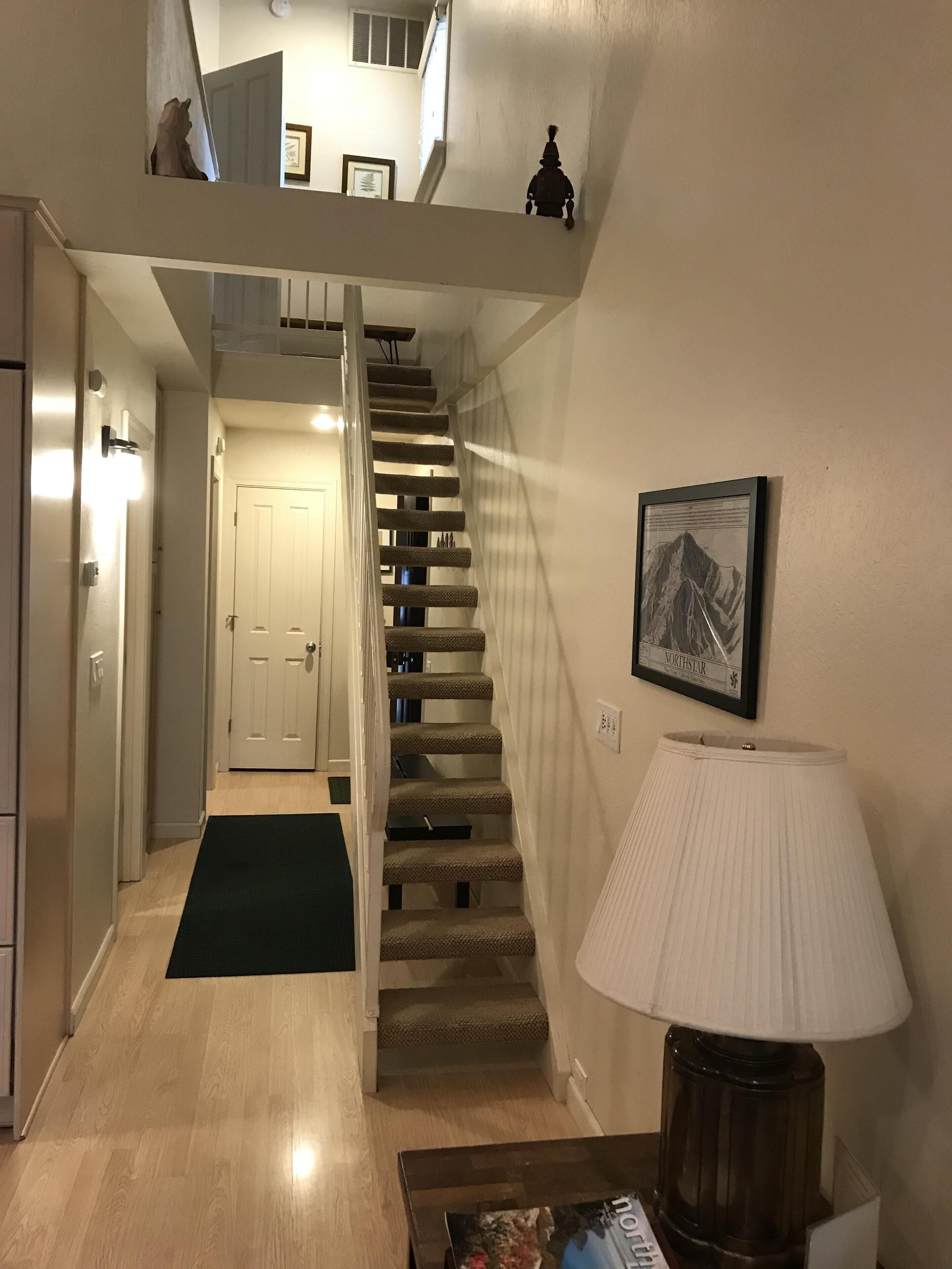 A staircase leading to an upper level, a framed picture on the wall, and a lamp on a table.